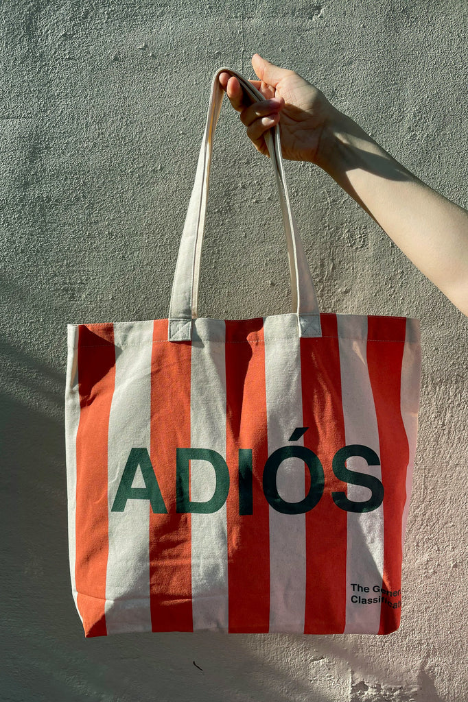 Tote bag with red and white stripes and 'ADIÓS' text held against a plain background