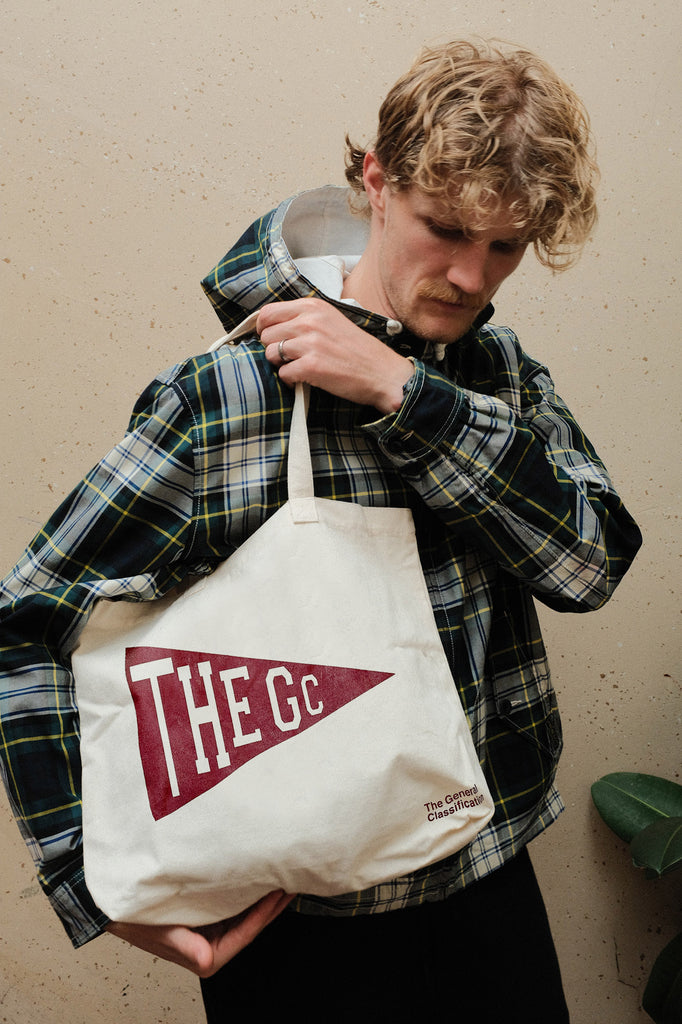 Person holding a tote bag with 'THE GC' logo against a plain background